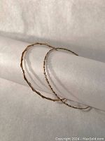 Two gold bangle bracelets draped over rolled white backdrop