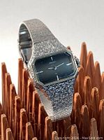 Front angled view showing octagonal silvertone case with dark dial and textured silvertone bracelet.