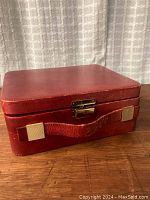 Closed red leather jewellery box showing exterior handle, brass latch and surface wear