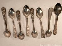 Eight silver-colored metal spoons laid out side by side, showing dragon designs on handles