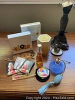 Assorted perfumes by Christina Aguilera, Estee Lauder, Bvlgari, mini perfume bottles, blue frosted atomizer, ring holder dress form, and black necklace stand on wood surface.