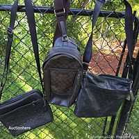 Three bags hanging on a fence outdoors: two black embossed Coach logo purses with adjustable shoulder/crossbody straps and one brown sling bag.