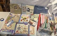 Overview photo showing multiple scrapbooking books, decorative papers, stickers, and bins with craft supplies arranged on a table.
