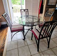 Full view of round glass dining table with four metal chairs with striped cushions around it, showing overall design and condition.