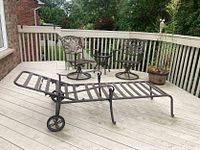 Full view of patio furniture showing lounger in foreground, two swivel chairs, and round table on a wooden deck.