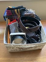 Photo of a fabric-lined box containing folded scarves, multiple belts, and other small accessories including a watch box.