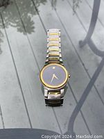 Front view of men's Movado wristwatch showing black dial, gold tone hands, and gold bezel.
