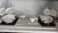 Two Villeroy & Boch New Wave coffee sets on display with cups and square saucers, along with the chrome caddies and other palette-shaped dishes in white porcelain.