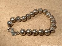 Photo showing the sterling silver ball bearing style bracelet laid flat, clasp and maker's tag visible.