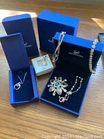 Photo showing multiple Swarovski jewelry pieces in blue Swarovski boxes on a wooden surface. Includes bracelets, necklaces, and a brooch.