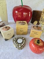 Photo showing large red ceramic apple vase, three square candles with copper lids each inscribed with inspirational words, heart-shaped pearl-accented candle holder, and ceramic apple container.