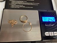 Three pieces of jewelry on a digital scale showing a total weight of 2.42 grams, jewelry includes a chain necklace, an engraved ring and a hoop earring with a pearl.