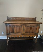 Front view of vintage dark oak sideboard showing carved door panels and turned legs.