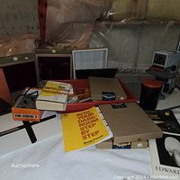 Wide shot showing assortment of vintage photography books, boxes, and darkroom supplies including film canisters and flash boxes on a white cloth surface.