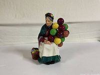 Front view of the Royal Doulton Old Balloon Seller porcelain figurine showing the elderly woman with colorful balloons and flower basket.