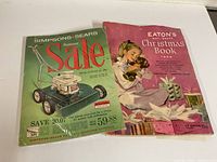 Photo of the front covers of two catalogues: green 1961 Simpsons-Sears Summer Sale and pink 1956 Eaton's Christmas Book.