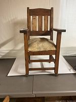 Front view of antique child's mission chair showing slatted back, broad armrests, and original hide cushion on seat.