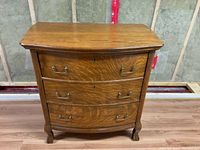 Full front view of the antique dresser showing its three drawers with metal handles, curved front, and claw feet.