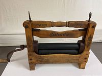 Side view of wooden clothes wringer showing the black covered cog wheels, branded Eatonia on the horizontal wooden bar, and metal crank handle.