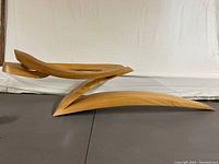 Side view of the wooden sculpture showing the elongated base and curved upper section with a hole in the middle.