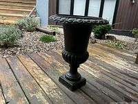 Side view of black metal planter urn showing decorative rim and classical urn profile with square base.