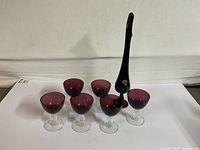 Wide front view showing six amethyst stemmed glasses and one tall black thumbprint Fenton bud vase