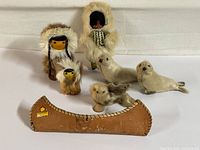 Two Native North American dolls, three small seal figurines, and miniature birch bark canoe placed on a flat surface, showcasing all items clearly for identification.