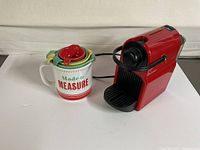Red Breville Nespresso coffee machine with black handle and accessories on side, next to colorful Jamie Oliver ceramic measuring cups set.