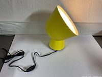 Yellow metal lamp with a conical adjustable shade angled forward, showing wired inline switch and cord.