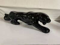 Side angle of the glossy black ceramic panther figurine showing muscular details and prowling position.