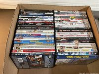View of 37 assorted DVD movies stacked in box showing various movie titles