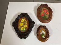 Three vintage Black Forest carved wooden oval frames with floral paintings, varying in size and wood tone.
