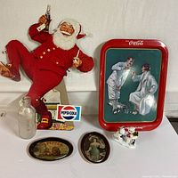 Full lot arranged on a table showing all items: cardboard Pepsi Santa, Coke tray, Pepsi bottle, two coasters, and bear decoration with penguin.