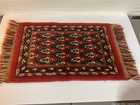 Full front view of the vintage carpet table mat showing the colorful pattern and fringes.