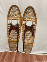 Pair of vintage cat gut snowshoes, showing front side with leather bindings, wooden frame, and woven cat gut lacing.