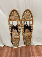 Full view of both vintage snowshoes showing wooden frames, cat gut lacing, and leather straps.