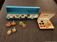 Overall photo showing multiple pairs of vintage cuff links including boxed sets and loose sets arranged on a dark surface.