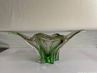 Front angled view of the vintage green glass bowl, showing flowing, wavy rim with purple hues.