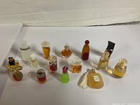 Photo showing 14 assorted vintage perfume bottle samplers arranged in a single line on a white surface with a beige background