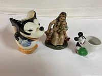 Front angle of all three items showing the Mickey Mouse creamer on left, Snow White figurine center, Mickey egg cup right.