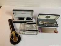 Photo showing entire lot including letter opener, two Sheaffer pens in cases, the glass base for letter opener, and Stik mechanical pencil.