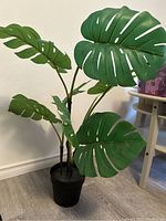 Front view of artificial monstera plant showing large split green leaves and black pot
