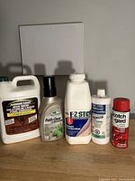 Five bottles of cleaning products placed on a wooden surface against a plain wall.