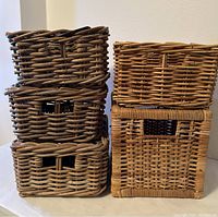 Front view of three dark brown woven wicker baskets stacked and two beige woven wicker baskets beside them.