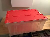 Photo showing the closed clear storage bin with red lid on a wooden surface.