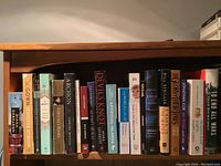 Books on a wooden shelf showing various titles and authors, mixed genres including fiction and non-fiction.