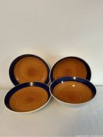 Four Italian ceramic bowls with a brown spiral interior and dark blue rim, white exterior, shown from top and side angles.