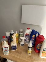 Photo of various bottles of cleaning products including Bona floor polish, Resolve carpet cleaner, Leak Stop can, and others on a floor against a wall.