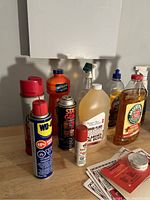 Photo of cleaning and maintenance supplies showing various bottles and cans arranged on wooden surface.