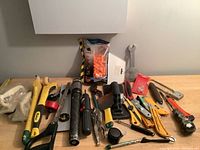 Photo showing assorted handyman tools including hammers, saws, cutters, wrenches, pliers, and orange foam ear plugs on a table.